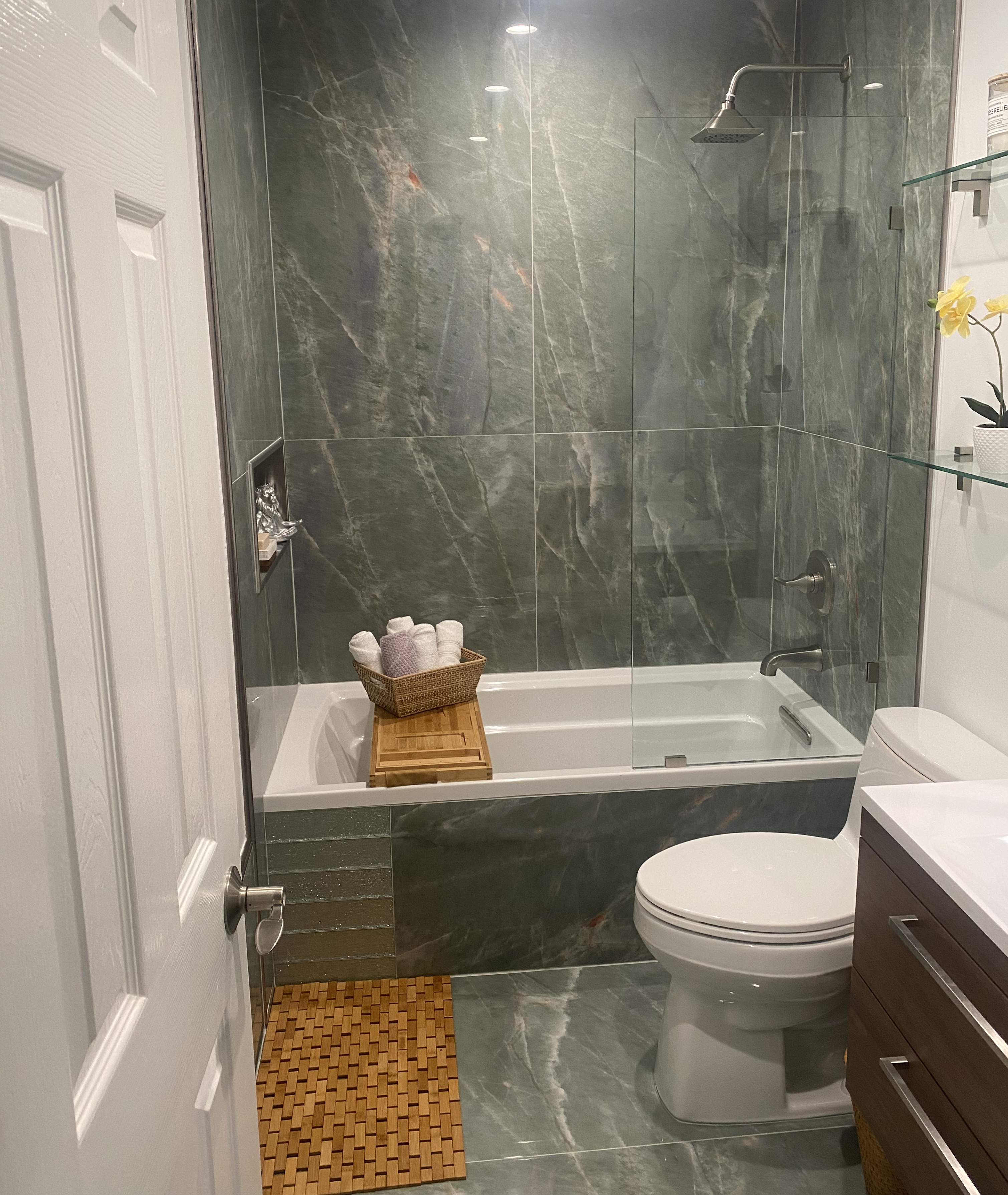Bathroom renovation with dark marble stone tile walls and glass partition
