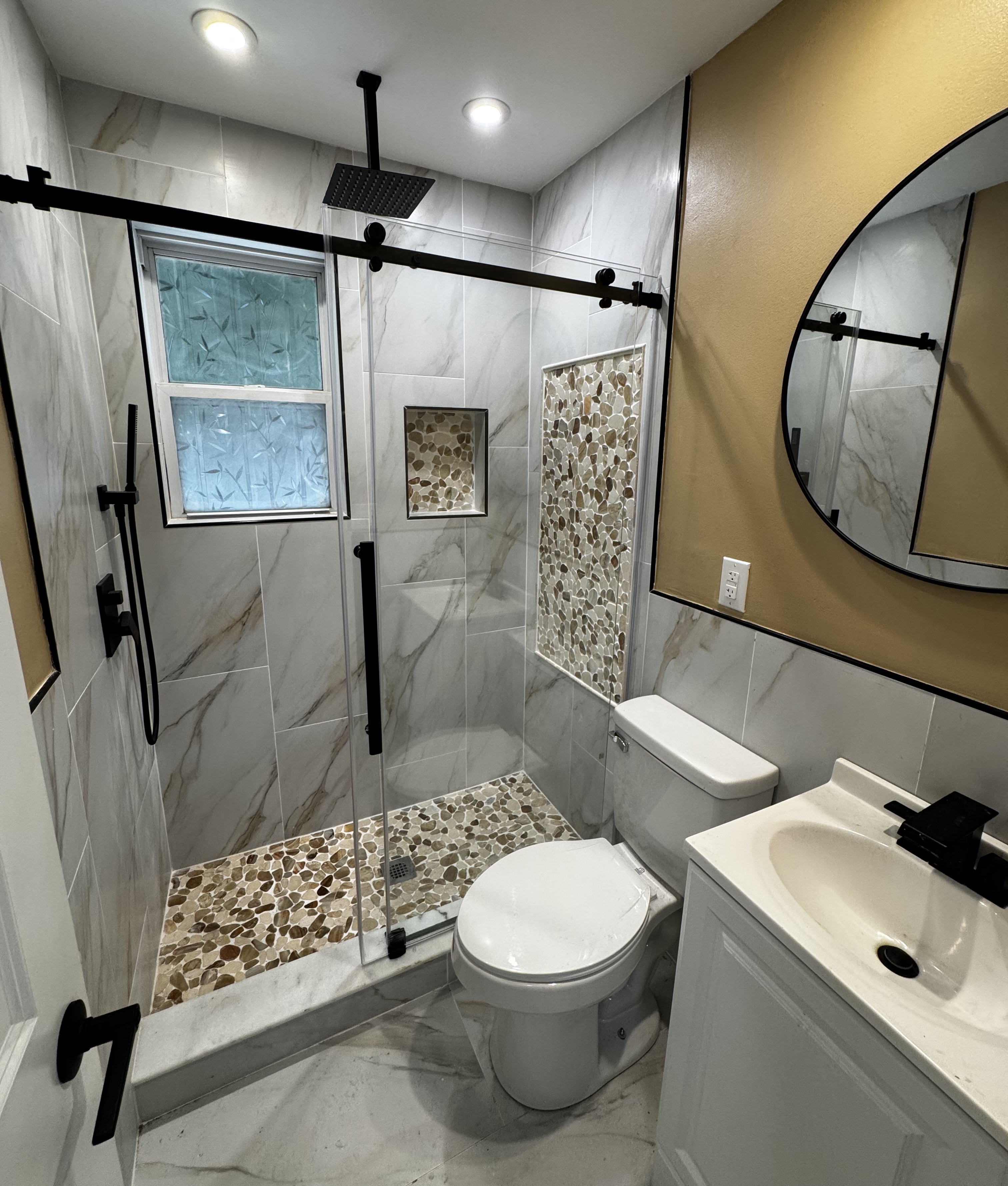 Modern bathroom with marble tile and pebble stone shower accents, glass door