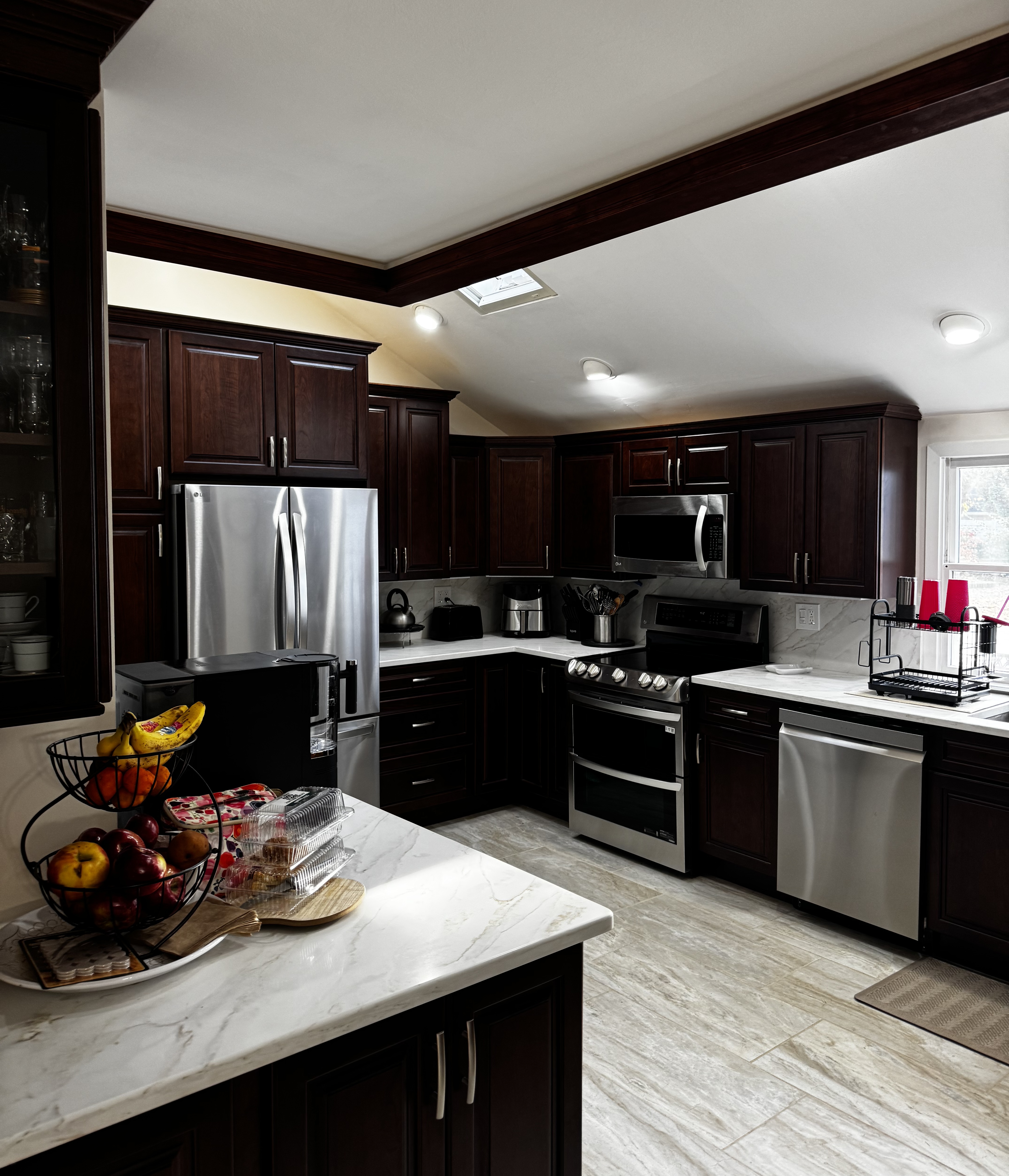 Kitchen renovation with dark wood cabinets, marble countertops, and stainless steel appliances